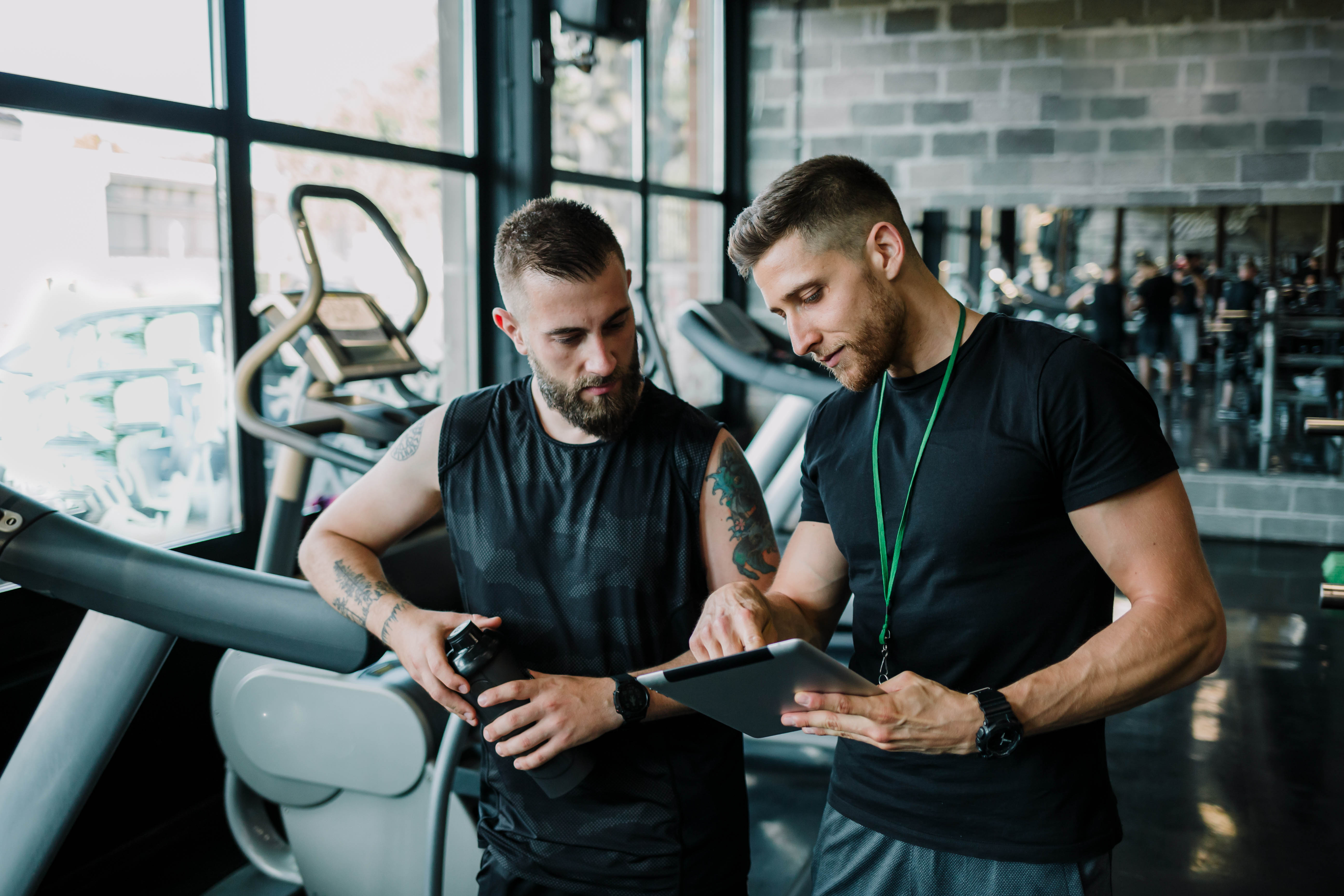 Male trainer meets with young, male client to discuss over a tablet in the gym Male trainer meets with young, male client to discuss over a tablet in the gym